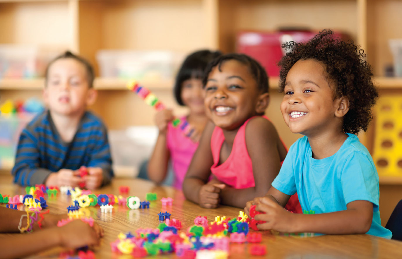 smiling students sitting at table with building toys